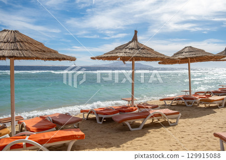 Relaxing beach view in Egypt with straw umbrellas and sun loungers by the serene blue sea 129915088