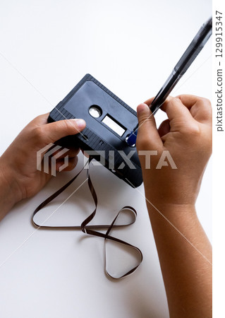 Hands adjusting cassette tape with pen for rewinding 129915347