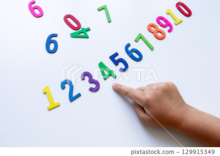 Child pointing at colorful wooden numbers on white background Child pointing at colorful wooden numbers on white background 129915349