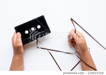 Child unraveling cassette tape on white background 129915356
