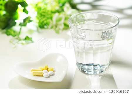 Tablets and capsules of medicine and a glass of mineral water 129916137