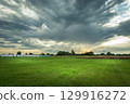 A rural view of gray rainy clouds over a green meadow on a summer day. 129916272