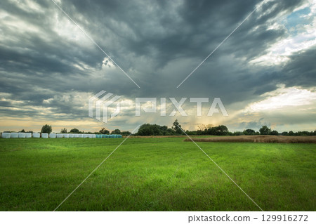 A rural view of gray rainy clouds over a green meadow on a summer day. A rural view of gray rainy clouds over a green meadow on a summer day. 129916272