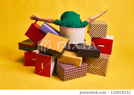 Child falling into pile of colorful shopping boxes on yellow background Child falling into pile of colorful shopping boxes on yellow background 129916532