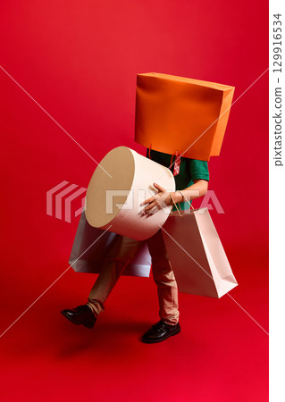 Child walking with large shopping bags and orange bag on head on red background 129916534