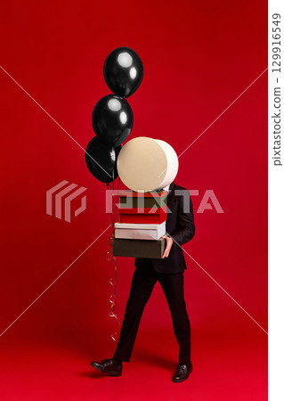 Person walking with gift boxes and black balloons on vivid red background 129916549
