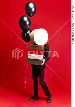 Person balancing boxes and black balloons while walking on red background Person balancing boxes and black balloons while walking on red background 129916550