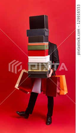 Person carrying boxes and paper shopping bags on red background Person carrying boxes and paper shopping bags on red background 129916553