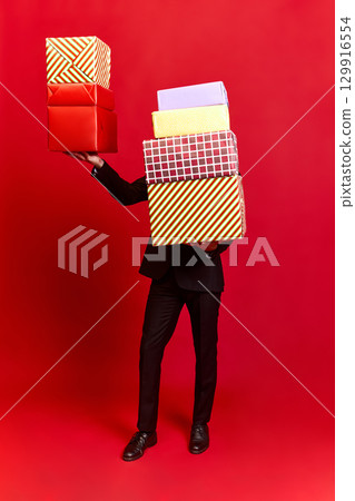 Person in black suit carrying colorful gift boxes on red background Person in black suit carrying colorful gift boxes on red background 129916554