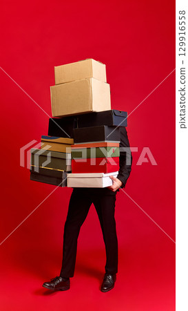 Person struggling to carry many stacked boxes on red background Person struggling to carry many stacked boxes on red background 129916558