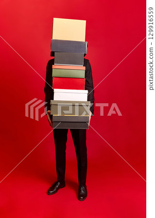 Person in black suit holding many boxes with hidden face on red background 129916559
