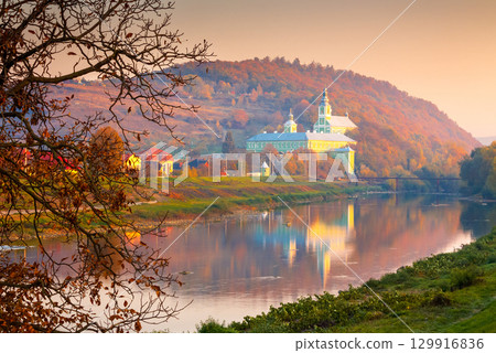 mukachevo, ukraine - 06 nov, 2015: urban landscape with river and trees in autumn. reflection of a monastery in the distance. beautiful travel destination of transcarpathia mukachevo, ukraine - 06 nov, 2015: urban landscape with river and trees in autumn. reflection of a monastery in the distance. beautiful travel destination of transcarpathia 129916836