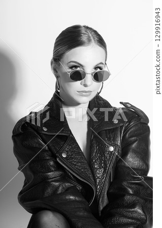 Woman black and white studio portrait with black punk leather jacket, sunglasses and without bra Woman black and white studio portrait with black punk leather jacket, sunglasses and without bra 129916943