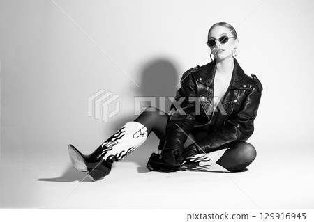 Woman black and white studio portrait with black punk leather jacket, sunglasses and without bra 129916945