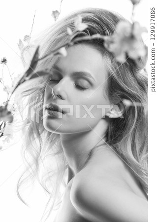 Beautiful woman with big wavy hair and flowers black and white studio portrait 129917086