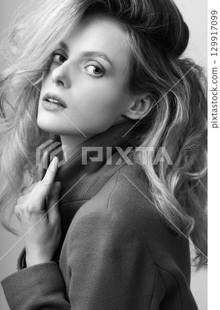 Beautiful woman with big wavy hair and garment coat studio portrait 129917099