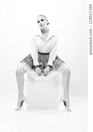 Beautiful woman with skirt sitting on white cube in white studio background Beautiful woman with skirt sitting on white cube in white studio background 129917169