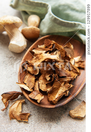 Dried porcini mushrooms resting in wooden bowl on gray textured background 129917899