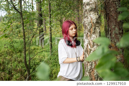 Young girl with pink hair exploring forest and touching tree trunk Young girl with pink hair exploring forest and touching tree trunk 129917910