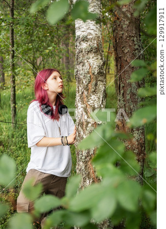 Young relaxed girl listening music leaning against birch in forest Young relaxed girl listening music leaning against birch in forest 129917911