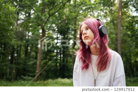 Young relaxed girl listening music with headphones in forest Young relaxed girl listening music with headphones in forest 129917912