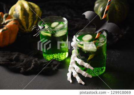 Halloween green cocktail garnish spider, black bat and pumpkins on black background. Festive drink and playful holiday decoration. Halloween green cocktail garnish spider, black bat and pumpkins on black background. Festive drink and playful holiday decoration. 129918069