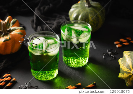 Halloween green cocktail garnish black bat and pumpkins on black background. Festive drink and playful holiday decoration. 129918075