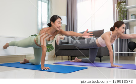 Two women practicing yoga in balancing table pose or Dandayamana Bharmanasana in living room at home 129918578