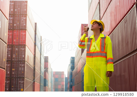 Asian man worker talking on walkie talkie for control loading containers box while standing in front of red containers at cargo shipping yard Asian man worker talking on walkie talkie for control loading containers box while standing in front of red containers at cargo shipping yard 129918580