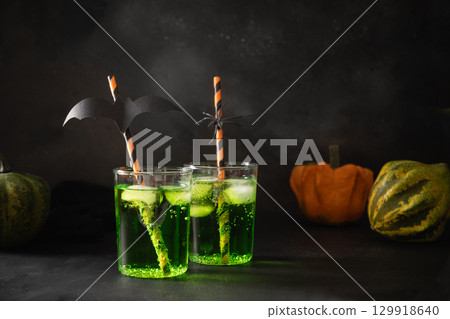 Halloween green cocktail garnish black bat and pumpkins on black background. Festive drink and playful holiday decoration. Halloween green cocktail garnish black bat and pumpkins on black background. Festive drink and playful holiday decoration. 129918640