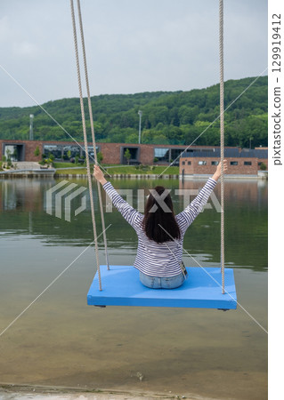 Person Relaxing on Swing by Scenic Lake Person Relaxing on Swing by Scenic Lake 129919412