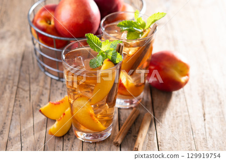 Refreshing peach iced tea in glass with ice cubes and cinnamon Refreshing peach iced tea in glass with ice cubes and cinnamon 129919754