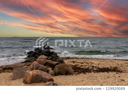 Waves crash over stones beneath a beautiful red sunset sea. 129920089