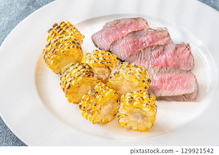 Juicy medium rare beef steak with roasted golden corn on white plate 129921542