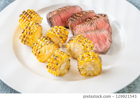 Juicy medium rare beef steak with roasted golden corn on white plate 129921543
