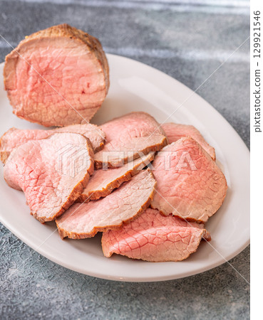 Perfectly sliced roast beef medium rare with seared crust on white plate 129921546