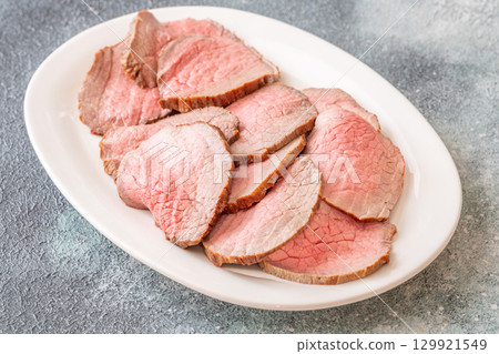 Perfectly sliced roast beef medium rare with seared crust on white plate 129921549