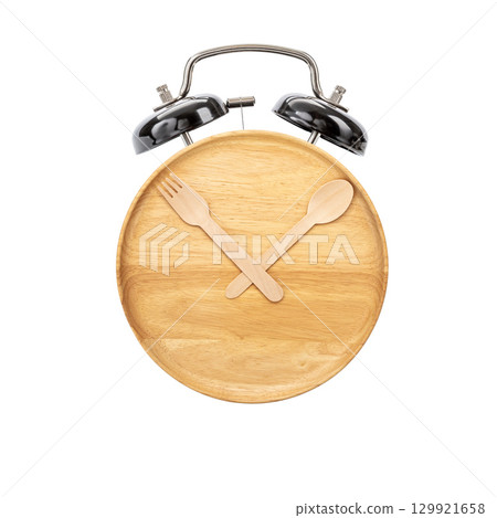 Wooden plate with fork and spoon arranged as clock hands, metal alarm clock bells on top, creative concept for meal time, isolated on white background Wooden plate with fork and spoon arranged as clock hands, metal alarm clock bells on top, creative concept for meal time, isolated on white background 129921658