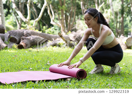 Yoga session outdoors. Young woman preparing yoga mat in serene park. 129922319