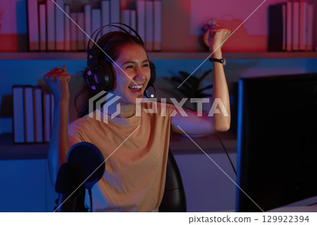 Excited Gamer Celebrating Win. Young woman with headset expressing joy during gaming. 129922394