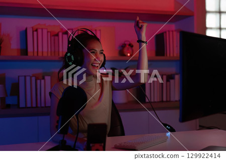 Gaming Excitement. Young woman celebrating a win in her gaming setup. Gaming Excitement. Young woman celebrating a win in her gaming setup. 129922414