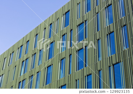 Modern office building facade with green panels and glass windows 129923135