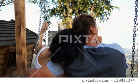 Romantic couple ride on swing together at sea beach. Happy lovers enjoy to spending time together at resort. Carefree pair enjoying rest near ocean at sunny day. Concept of summer vacation or holiday 129923374