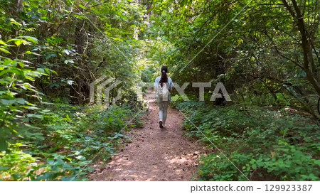Young woman going along path at summer forest. Female with backpack walking among trail at wild nature. Unrecognizable girl enjoying stroll outdoor admiring beautiful scenic. Close up Rear view 129923387