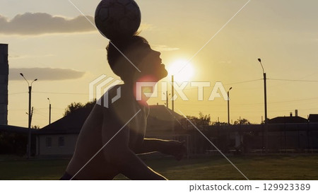 Young man juggling soccer ball on stadium at sunset. Professional footballer kicking ball at green field. Sportsman practicing tricks at meadow with sunlight at background. Freestyle football 129923389