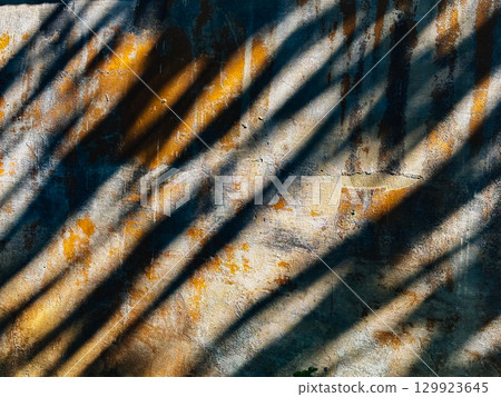 Abstract textured wall with striking shadows from the sun, creating a visual contrast. The textured wall, sun-drenched, creates a play of light and shadow, highlighting the architectural details. 129923645