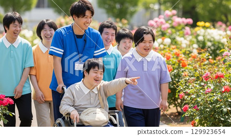 一名坐在輪椅上的殘障男子和他的護工在公園玫瑰園裡微笑著的照片 129923654