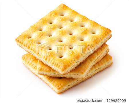 A close-up shot of a small pile of square creme crackers stacked against a plain white background. The crackers are golden-brown with small holes on their surface. 129924009