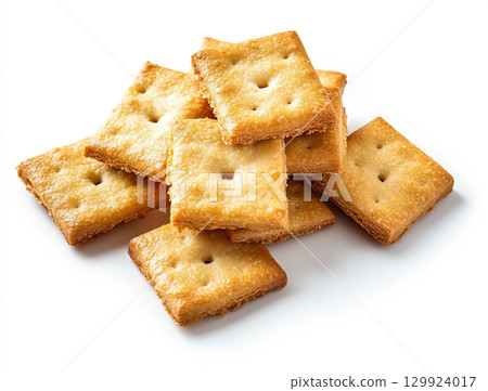 A close-up shot of a small pile of square creme crackers stacked against a plain white background. The crackers are golden-brown with small holes on their surface. 129924017