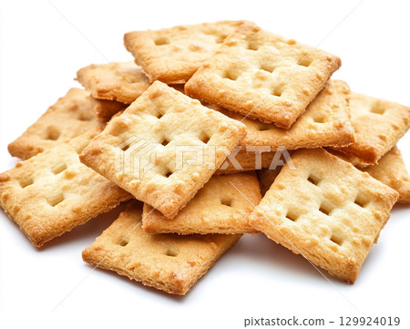 A close-up shot of a small pile of square creme crackers stacked against a plain white background. The crackers are golden-brown with small holes on their surface. 129924019